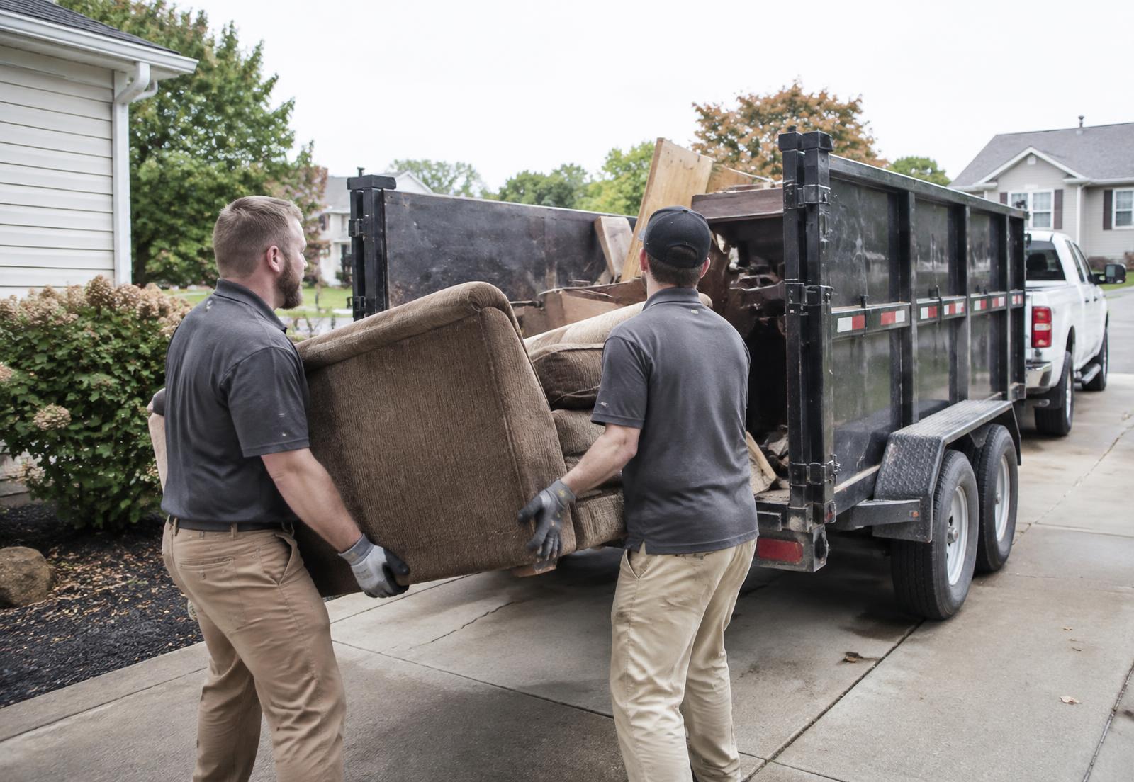 Junk removal in Peoria, IL — Lance Junk Removal crew loading an old couch into a dump trailer